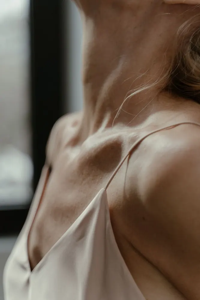 Gros plan sur une clavicule et la fine bretelle d'une nuisette en satin.