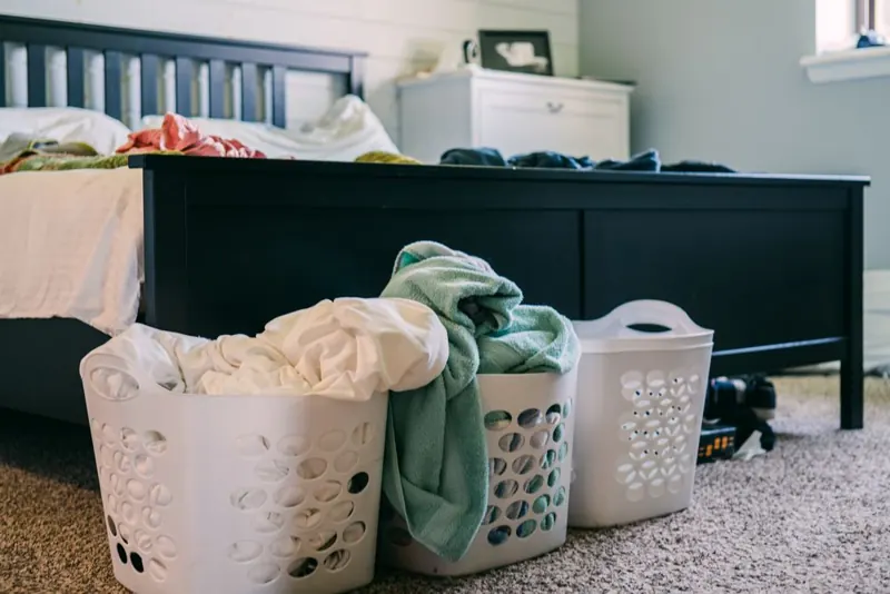 Chambre en désordre : paniers de linge au pied du lit, vêtements sur la couette.
