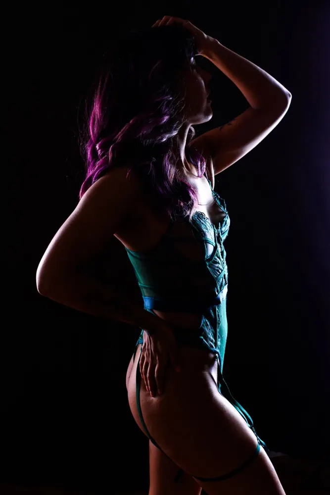 Femme en lingerie de profil, une main dans les cheveux, l'autre sur la hanche, sa silhouette soulignée par une lumière venue de derrière.