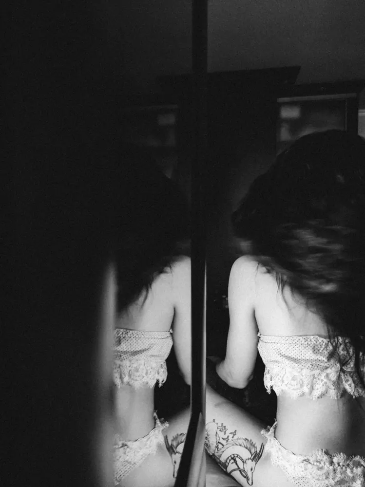 Photo en noir et blanc : une femme en lingerie de dentelle, de dos, et son reflet dans un miroir.